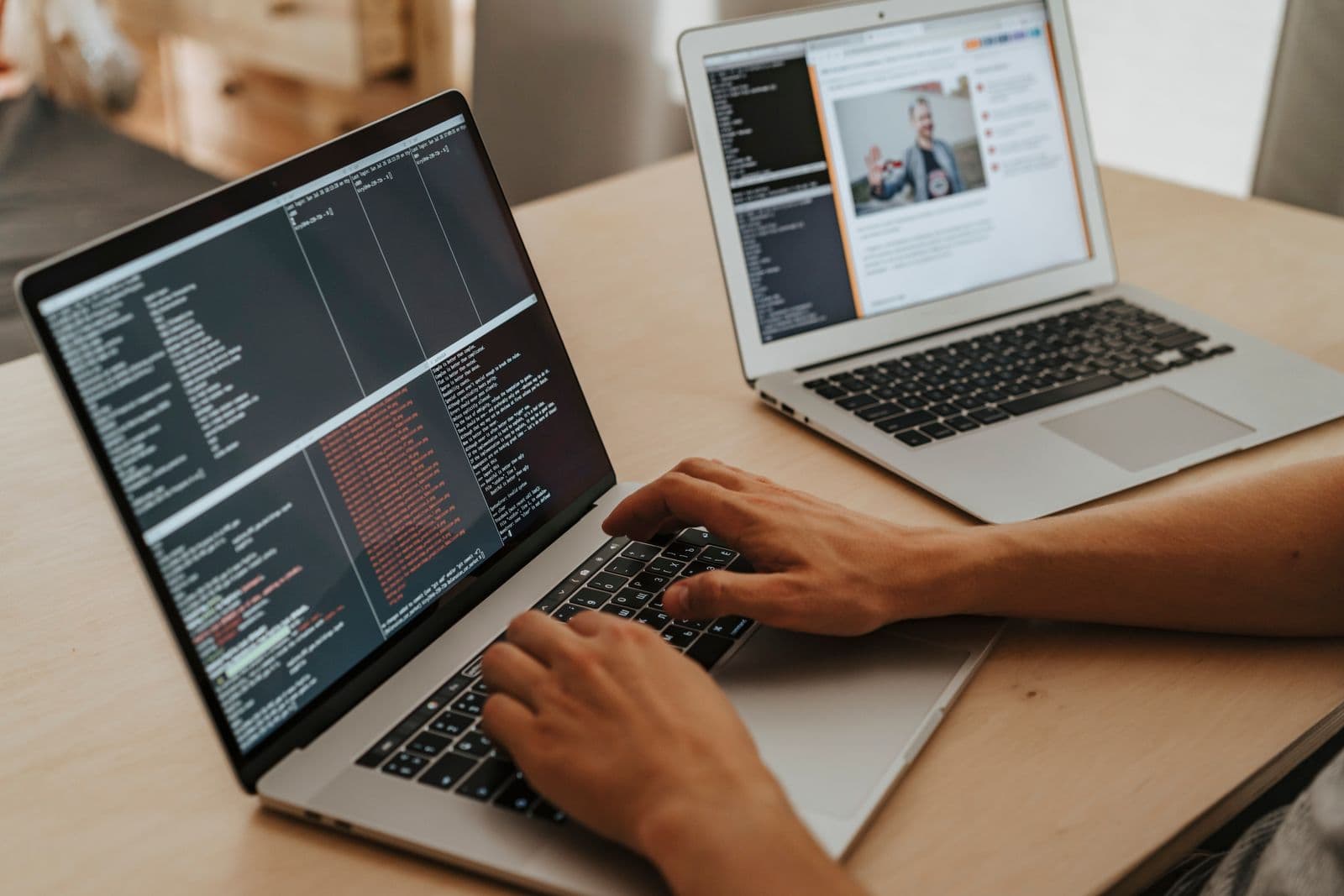A developer working across two laptops with code on screen